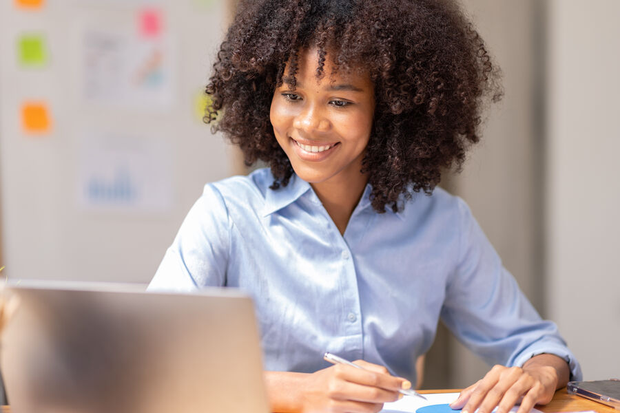 A woman at a laptop in an office, tired half-smile