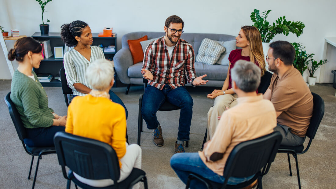 A diverse circle of adults sitting together in a sunlit room, listening attentively to one another